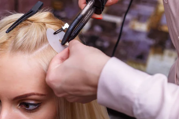 Procedura de extensie a părului. Coafeza face extensii de păr pentru o fată tânără, blondă într-un salon de înfrumusețare. Focalizare selectivă . — Fotografie, imagine de stoc