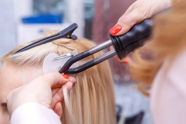 Procedura di estensione capelli. Il parrucchiere fa prolungamenti di capelli a ragazza giovane, bionda in un salone di bellezza. Focus selettivo . — Foto Stock