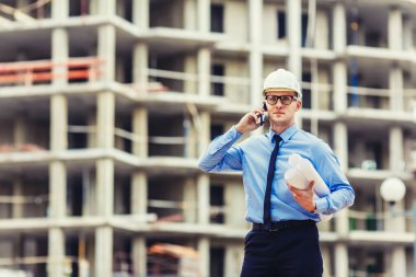 İnşaat mühendisi inşaat sahasında kameraya bakarak ve mobilephone konuşuyor