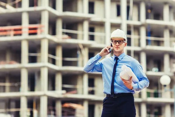 İnşaat mühendisi inşaat sahasında kameraya bakarak ve mobilephone konuşuyor