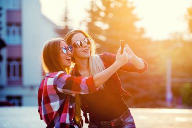 Selfie fotoğraf Smartphone'da yapmak mutlu iki gülümseyen kız portresi. kentsel arka plan. Akşam güneşin şehri.