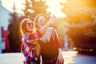 Selfie fotoğraf Smartphone'da yapmak mutlu iki gülümseyen kız portresi. kentsel arka plan. Akşam güneşin şehri.
