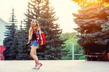 Genç güzel hipster kadın uzun saçlı ve güneşli yaz sokak kırmızı sırt çantası açık moda portre. Akşam güneşin şehri.