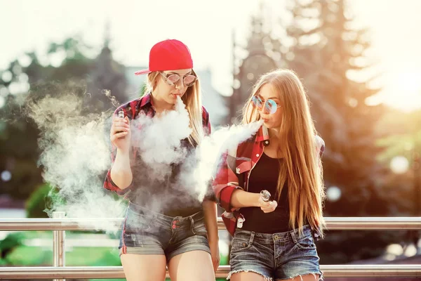 Duas mulheres a vaporizar ao ar livre. O pôr-do-sol da noite sobre a cidade. Imagem tonificada . — Fotografia de Stock