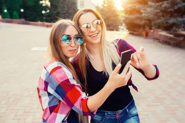 Portrét šťastný dvě usmívající se dívky které selfie foto na smartphone. městské pozadí. Večerní slunce nad městem. — Stock fotografie