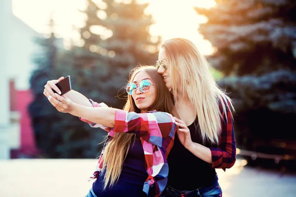 Ritratto di una felice due ragazze sorridenti fare foto selfie su smartphone. sfondo urbano. Il tramonto serale sulla città . — Foto Stock