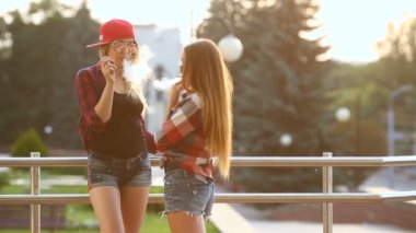 İki kadın vaping açık. Akşam güneşin şehri. Tonlu görüntü.