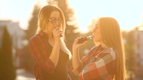 Dos mujeres vapeando al aire libre. La puesta de sol de la noche sobre la ciudad. Imagen tonificada . — Vídeos de Stock