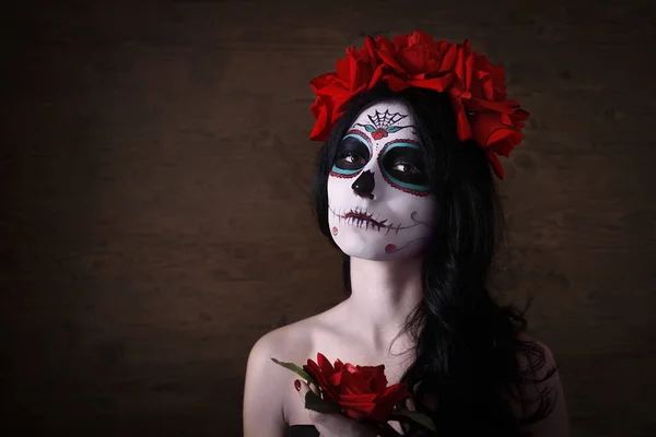 El día de los muertos. Halloween. Mujer joven en el día de la máscara muerta cráneo cara arte y rosa. Fondo oscuro . Fotos de stock libres de derechos