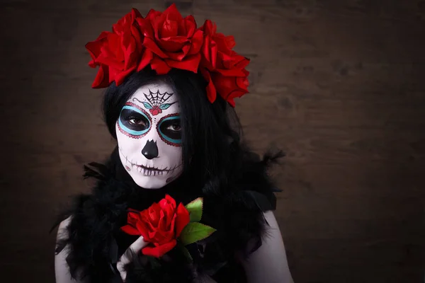 死亡日。万圣节.年轻的女人在死去的面具骷髅脸上画着玫瑰。深色背景. 图库照片