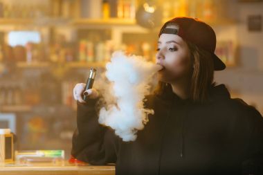 Genç kadın kırmızı bere duman elektronik sigara vape dükkanında güzel. Hip-hop tarzı. Portre.