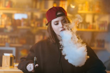 Genç kadın kırmızı bere duman elektronik sigara vape dükkanında güzel. Hip-hop tarzı. Portre.