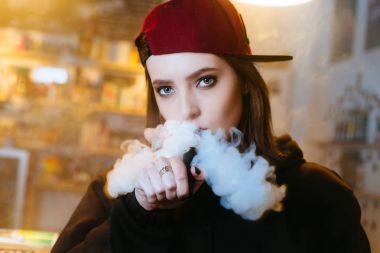 Genç kadın kırmızı bere duman elektronik sigara vape dükkanında güzel. Hip-hop tarzı. Portre.