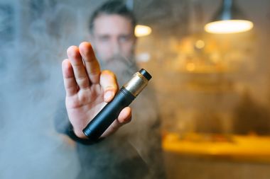 Genç adam Haritayı vaping aygıt uzanmış elinde Buhar bulutu aracılığıyla sakallı. Seçici odak. Vaping kavramı. Kopya alanı.