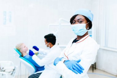 Genç Afro-Amerikan kadın diş hekimi diş hekimi diş kliniğinde hastaya kontrol önünde maskeli. Diş Kliniği kavramı.