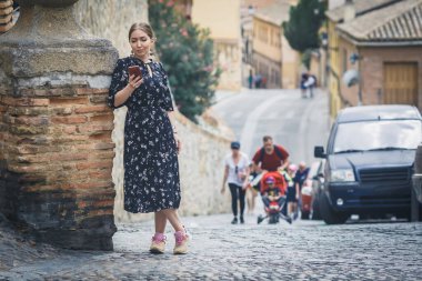 Eski kasaba caddesinde akıllı telefon kullanan siyah elbiseli güzel bir genç kadın. Avrupa seyahati.