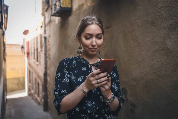 Pretty young woman in a black dress using smartphone at old town street. Travel by Europe. Toledo, Spain — Stock Photo, Image
