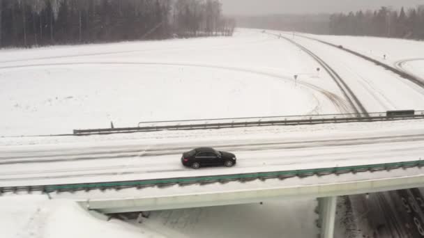車は橋に乗る。冬の田舎道で車の運転、 4kのドローンからの空中ビュー。トラッキングショット. — ストック動画