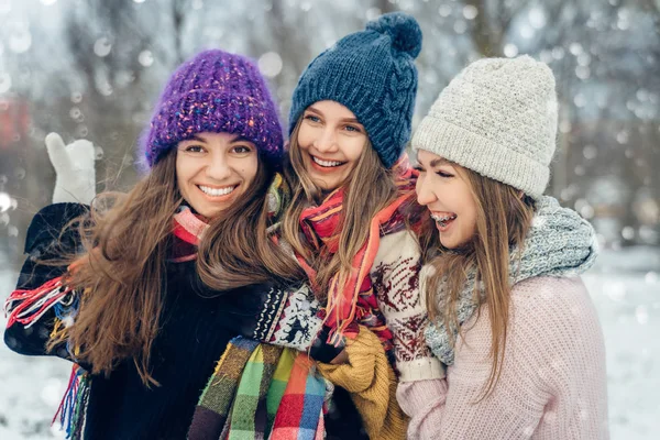 Three women friends outdoors in knitted hats having fun on a snowy cold weather. Group of young female friends outdoors in winter park.