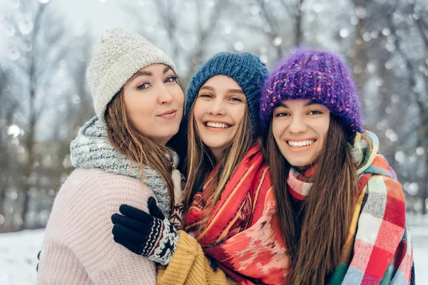 Three women friends outdoors in knitted hats having fun on a snowy cold weather. Group of young female friends outdoors in winter park.