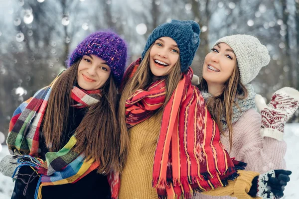 Drei Freundinnen in Strickmützen amüsieren sich bei schneereicher Kälte. Gruppe junger Freundinnen im Winterpark. — Stockfoto