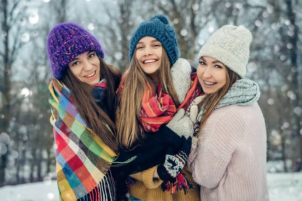 Τρεις γυναίκες φίλοι σε εξωτερικούς χώρους με πλεκτά καπέλα διασκεδάζουν σε ένα χιονισμένο κρύο καιρό. Ομάδα νεαρών γυναικών σε εξωτερικούς χώρους στο χειμερινό πάρκο. — Φωτογραφία Αρχείου