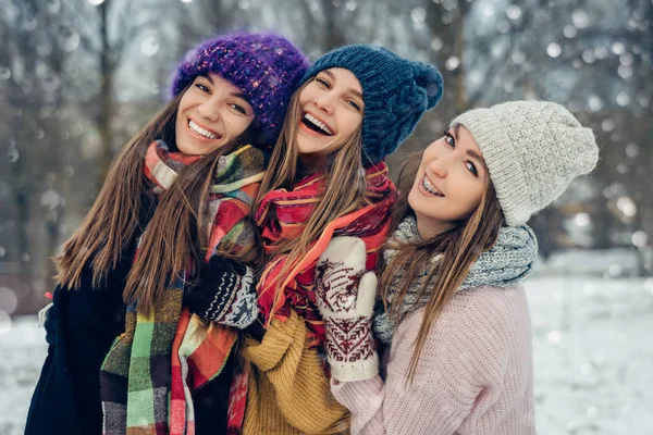 Tre amiche all'aperto in cappelli lavorati a maglia che si divertono su un freddo nevoso. Gruppo di giovani amiche all'aperto nel parco invernale . — Foto Stock