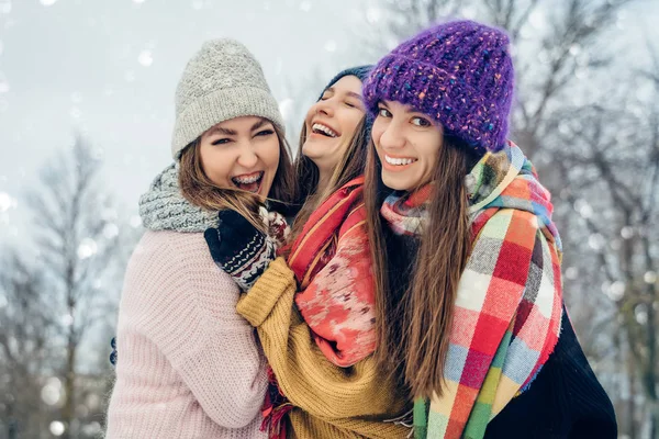 Três mulheres amigas ao ar livre em chapéus de malha se divertindo em um tempo frio nevado. Grupo de jovens amigas ao ar livre no parque de inverno . — Fotografia de Stock