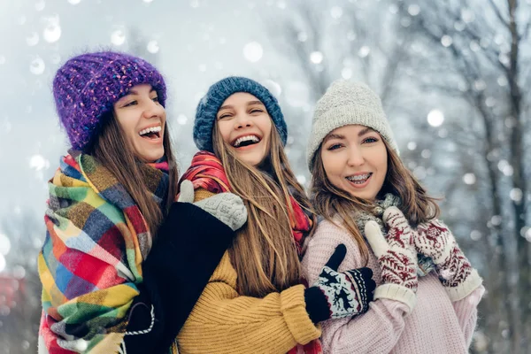 Τρεις γυναίκες φίλοι σε εξωτερικούς χώρους με πλεκτά καπέλα διασκεδάζουν σε ένα χιονισμένο κρύο καιρό. Ομάδα νεαρών γυναικών σε εξωτερικούς χώρους στο χειμερινό πάρκο. — Φωτογραφία Αρχείου