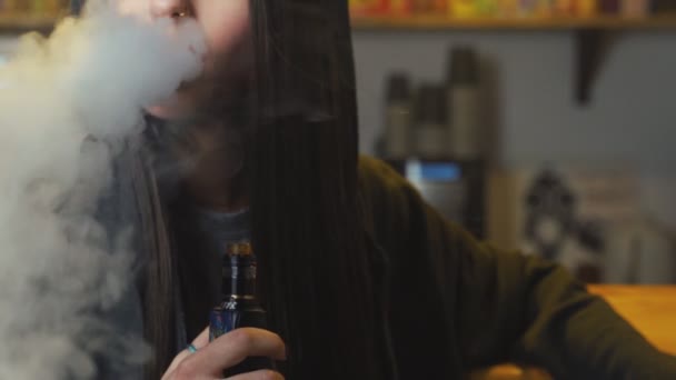 Молода красива жінка в кепці курить електронну сигарету у вейп-шопі. Стиль хіп-хоп. крупним планом . — стокове відео