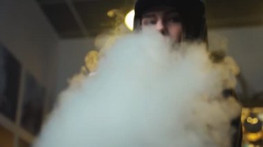Şapkalı genç bir kadın vape dükkanında elektronik sigara içiyor. Hip-hop tarzı. Yakın çekim..