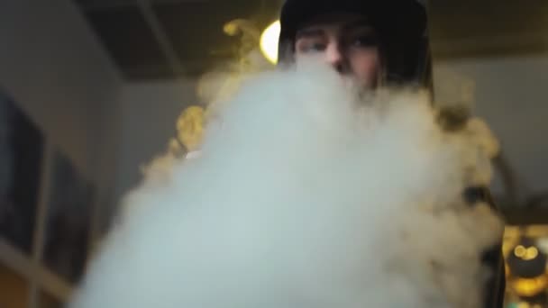 Young pretty woman in cap smoke an electronic cigarette at the vape shop. Hip-hop style. Closeup. — Stock Video