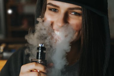 Şapkalı genç bir kadın vape dükkanında elektronik sigara içiyor. Hip-hop tarzı. Yakın çekim..