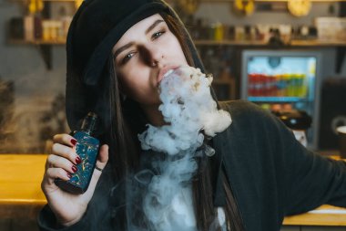Şapkalı genç bir kadın vape dükkanında elektronik sigara içiyor. Hip-hop tarzı. Yakın çekim..