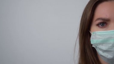 Kadının yüzünün yarısı Coronavirus ya da Covid-19 'u korumak için maske takıyor. Koruyucu maskeli genç bir kadın kameraya bakıyor..