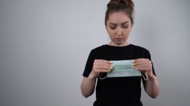 Maske takan ve beyaz arka planda kameraya bakan bir kadın. Koruyucu maske takan Avrupalı genç bir kadının pandemik, kırpılmış portresi. Coronavirus konsepti. Sağlık ve Sağlık Hizmetleri.