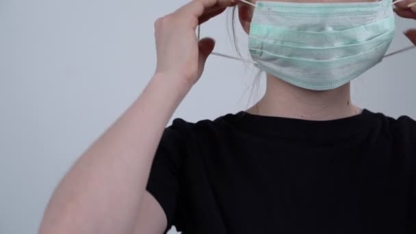 Femme portant un masque et regardant la caméra sur fond blanc. Portrait pandémique et recadré d'une jeune femme européenne portant un masque protecteur. Concept de coronavirus. Soins de santé et médicaux . — Video