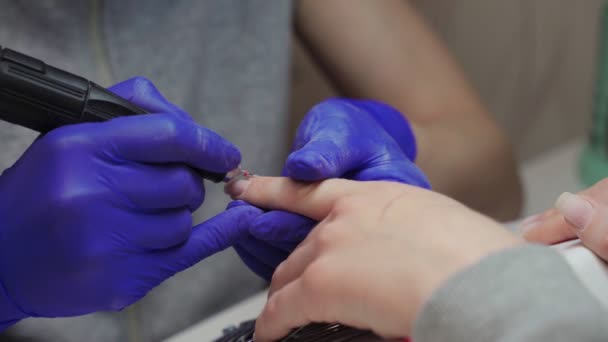 Žena manikúra mistr v modrých rukavicích v salonu krásy zpracovává kůžičku na nehty klienta pomocí manikúry stroj. — Stock video