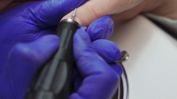 Vrouwelijke manicure meester in blauwe handschoenen in de schoonheidssalon verwerkt de nagel op de nagels van de klant met behulp van een manicure machine. — Stockvideo