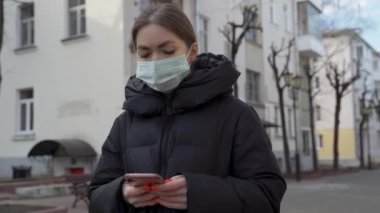 Avrupa sokaklarında akıllı telefon kullanan koruyucu tıbbi maskeli bir kadının portresi. Sağlık ve güvenlik, N1H1 koronavirüs, covid-19, virüs koruma ve tıbbi konsept. Sağa çevir.