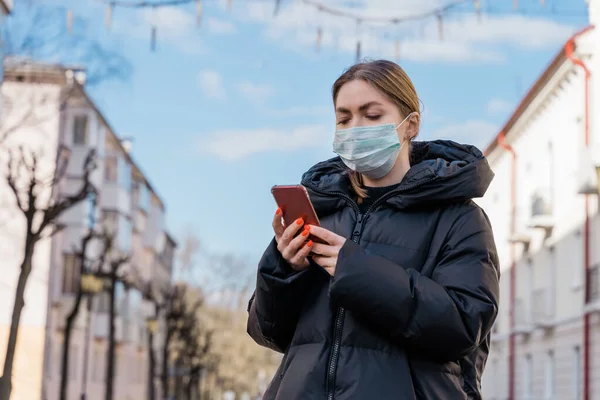 Avrupa sokaklarında akıllı telefon kullanan koruyucu tıbbi maskeli bir kadının portresi. Sağlık ve güvenlik, N1H1 koronavirüs, covid-19, virüs koruma ve tıbbi konsept. Sol tarafı çevir.