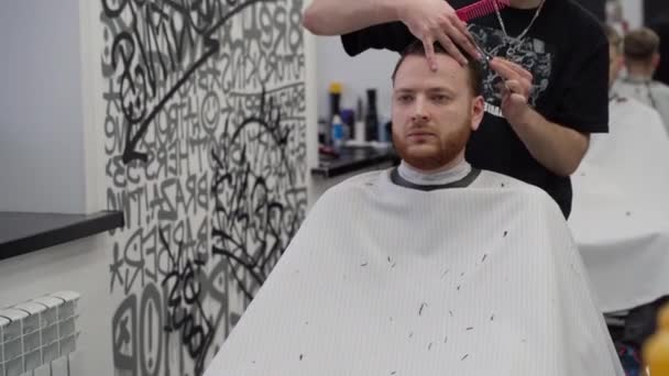 Il barbiere taglia i capelli del cliente con le forbici. Chiudete. Maschio attraente sta ottenendo un taglio di capelli moderno in negozio di barbiere. Colpo in mano. 4K. — Video Stock