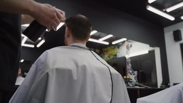 Barbeiro molha o cabelo por spray e penteia-los. Um homem atraente está a cortar o cabelo na barbearia. Tiro portátil . — Vídeo de Stock