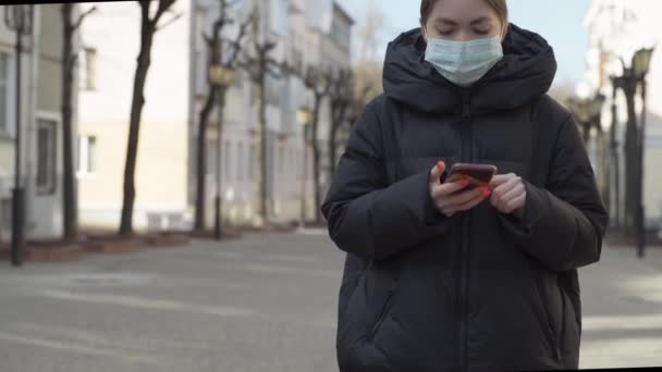 Pportrait of woman in protective medical mask using smart phone on empty european streets. Health and safety, N1H1 coronavirus, covid-19, virus protection care and medical concept. Tilt up shot. — Stock Video