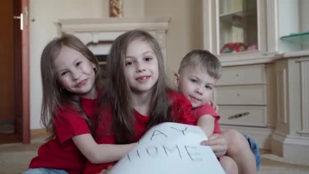 Familie bleibt zu Hause. Drei Kinder, die ein Schild mit der Aufschrift "Bleiben Sie zum Virenschutz zu Hause und kümmern Sie sich um Ihre Gesundheit von COVID-19. — Stockvideo