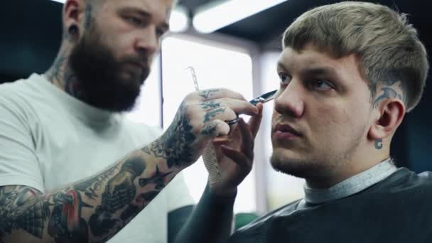 Барбер підстригає волосся клієнта ножицями. Закрийся. У перукарні привабливий самець підстригається. Постріл у кишеню. 4K. — стокове відео