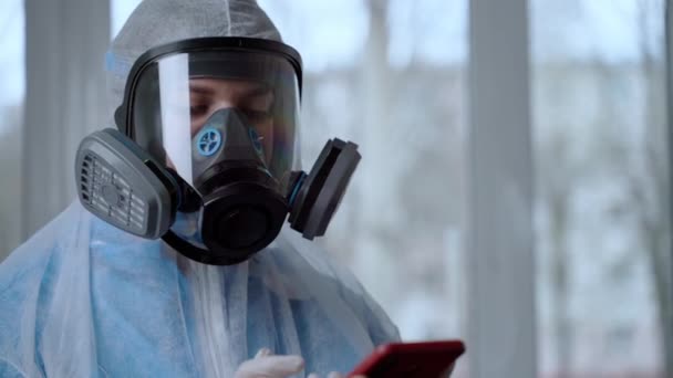 Female Doctor Wearing a Facemask and Suit sand informatiom by mobile phone. Medic wears a protective suit and mask during the COVID19 outbreak. Coronavirus pandemic concept — Stock Video