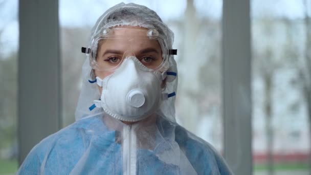 Portret van een vrouwelijke arts die beschermende kleding weert tijdens een coronavirus pandemie. Vermoeide vrouwelijke arts in gevarenpak, ademhalingsmasker, handschoenen en bril na werkdag in kliniek of ziekenhuis — Stockvideo