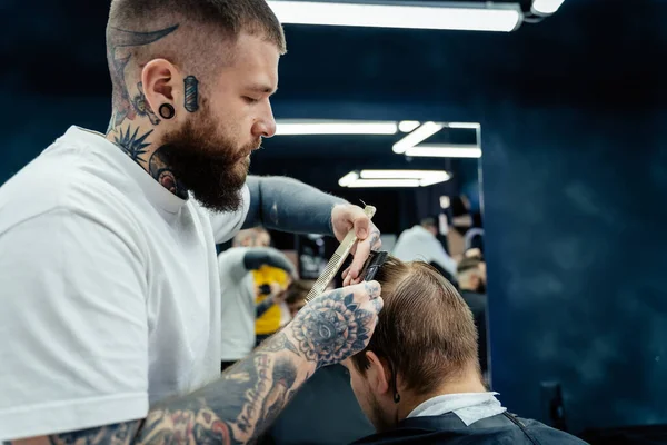 Professioneller tätowierter Friseur mit rasiermesserscharfen Haaren. Attraktive Männer bekommen im Friseursalon einen modernen Haarschnitt. Nahaufnahme. — Stockfoto