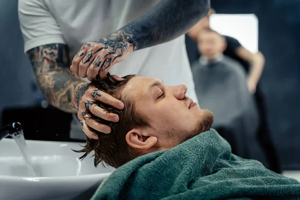 Attraktive Männer bekommen im Friseursalon einen modernen Haarschnitt. Draufsicht eines jungen Mannes, der sich in einem Friseursalon die Haare wäscht und den Kopf massiert — Stockfoto
